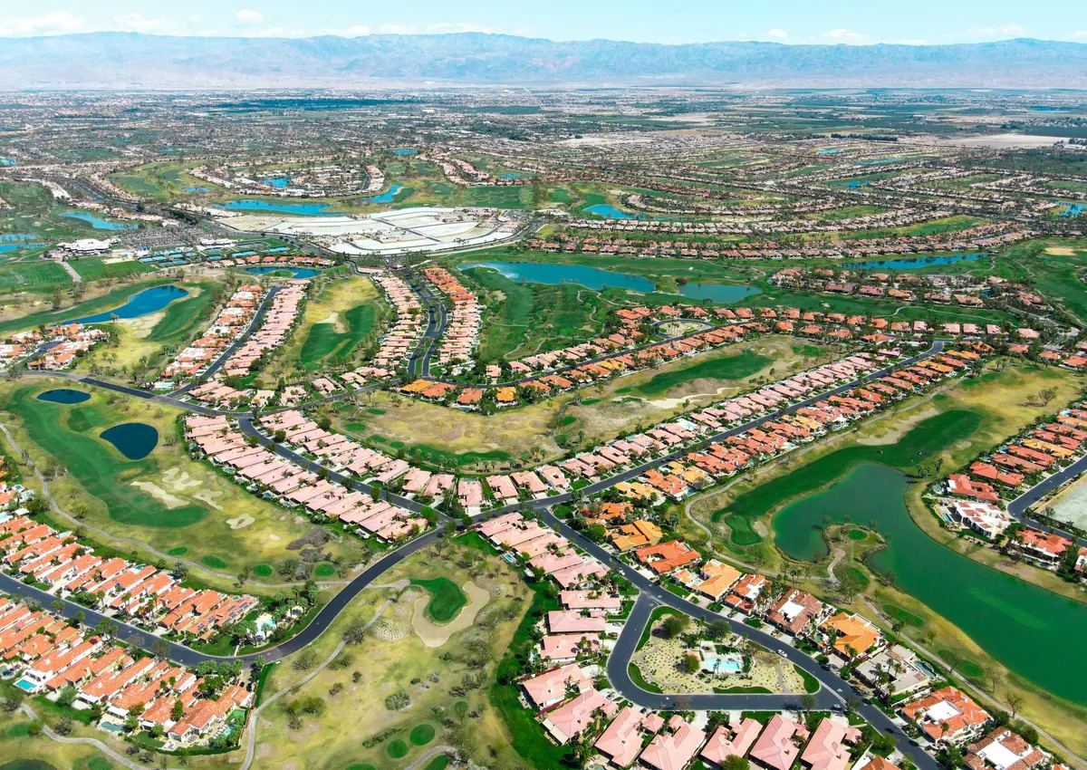 Aerial view of a golf-course community with red-tile roofs below the mountains